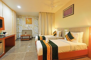 A hotel room with two beds, a desk, a television, and a ceiling fan. - Hotel Silk City (Varanasi)