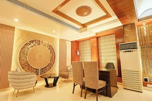 A modern interior with a round decorative wall, two sofas, a dining table, and a built-in air conditioning unit. - Hotel Silk City (Varanasi)
