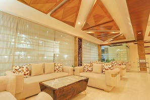 A modern living room with a sectional sofa, a coffee table, and a decorative wooden ceiling. - Hotel Silk City (Varanasi)