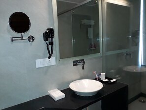Un baño moderno con un espejo redondo, un teléfono negro, una caja de pañuelos blancos y un lavabo grande de color blanco.