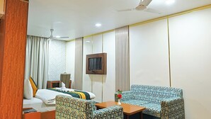 A hotel room with a bed, two patterned sofas, a TV, and a ceiling fan. - Hotel Silk City (Varanasi)
