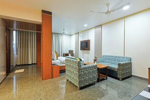 A hotel room with a bed, a sofa, a TV, and a ceiling fan. - Hotel Silk City (Varanasi)