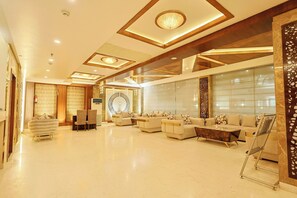 A spacious lobby with a modern design, featuring a seating area with sofas and a coffee table, a large decorative wall, and a patterned floor. - Hotel Silk City (Varanasi)