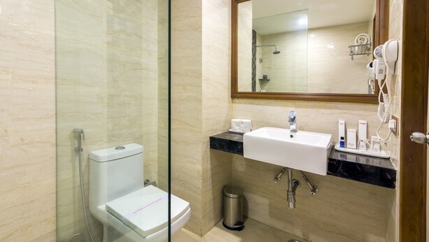 Un baño con ducha envuelta en vidrio, un inodoro blanco, un lavabo con encimera de mármol y un espejo sobre el lavabo.