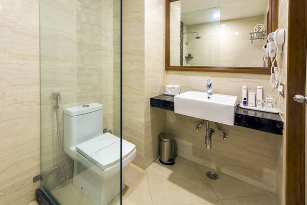 Un baño con ducha envuelta en vidrio, un inodoro blanco, un lavabo con encimera de mármol y un espejo sobre el lavabo.