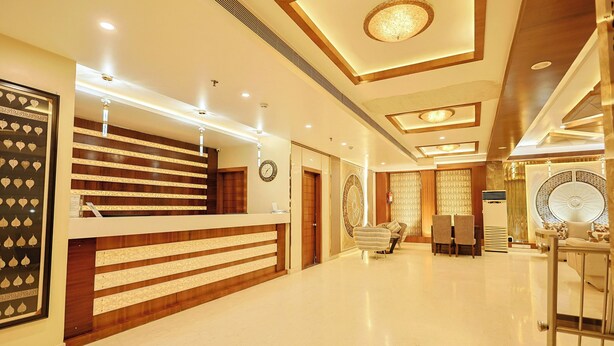 A hotel reception area with a reception desk, a clock, and a seating area with chairs. - Hotel Silk City (Varanasi)