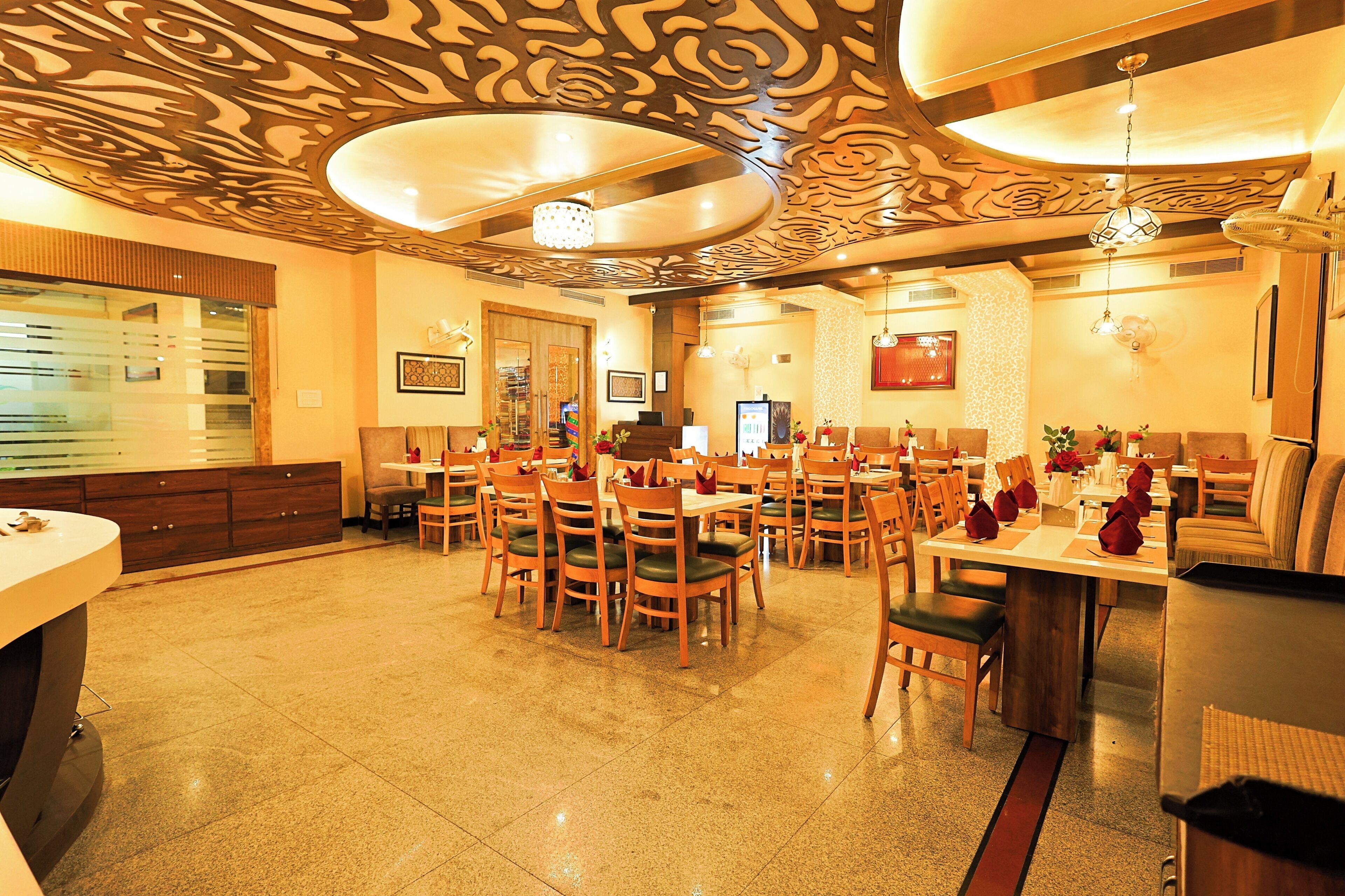 A restaurant with a patterned ceiling, wooden chairs, and tables set for dining.