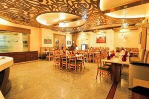 A restaurant with a patterned ceiling, wooden chairs, and tables set for dining. - Hotel Silk City (Varanasi)