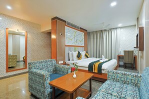 A hotel room with a bed, two sofas, a table, a mirror, and a painting. - Hotel Silk City (Varanasi)