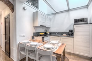 A modern kitchen with white cabinets, a dining area with a wooden table and white chairs, a built-in microwave, and a skylight above the kitchen. - Signoria Elegant by Mmega (Florence)