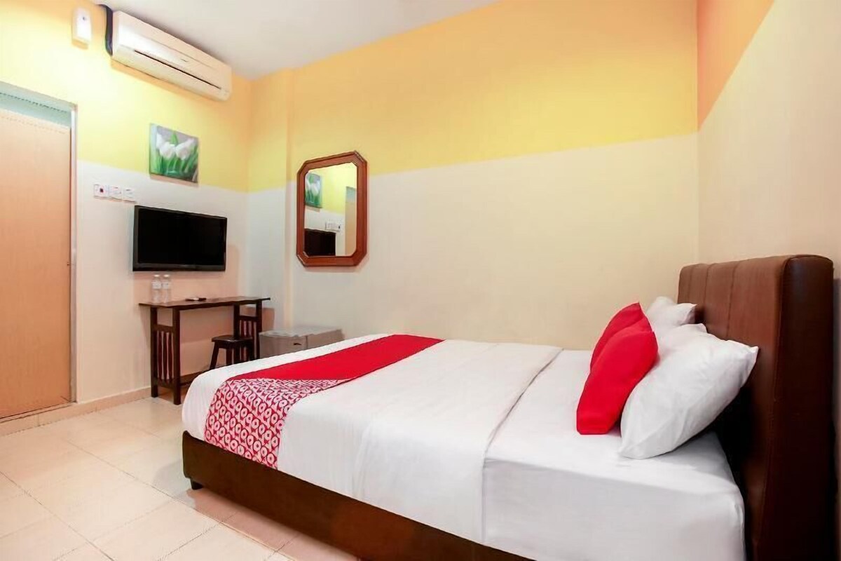 A hotel room with a bed, a desk, a television, and an air conditioning unit.