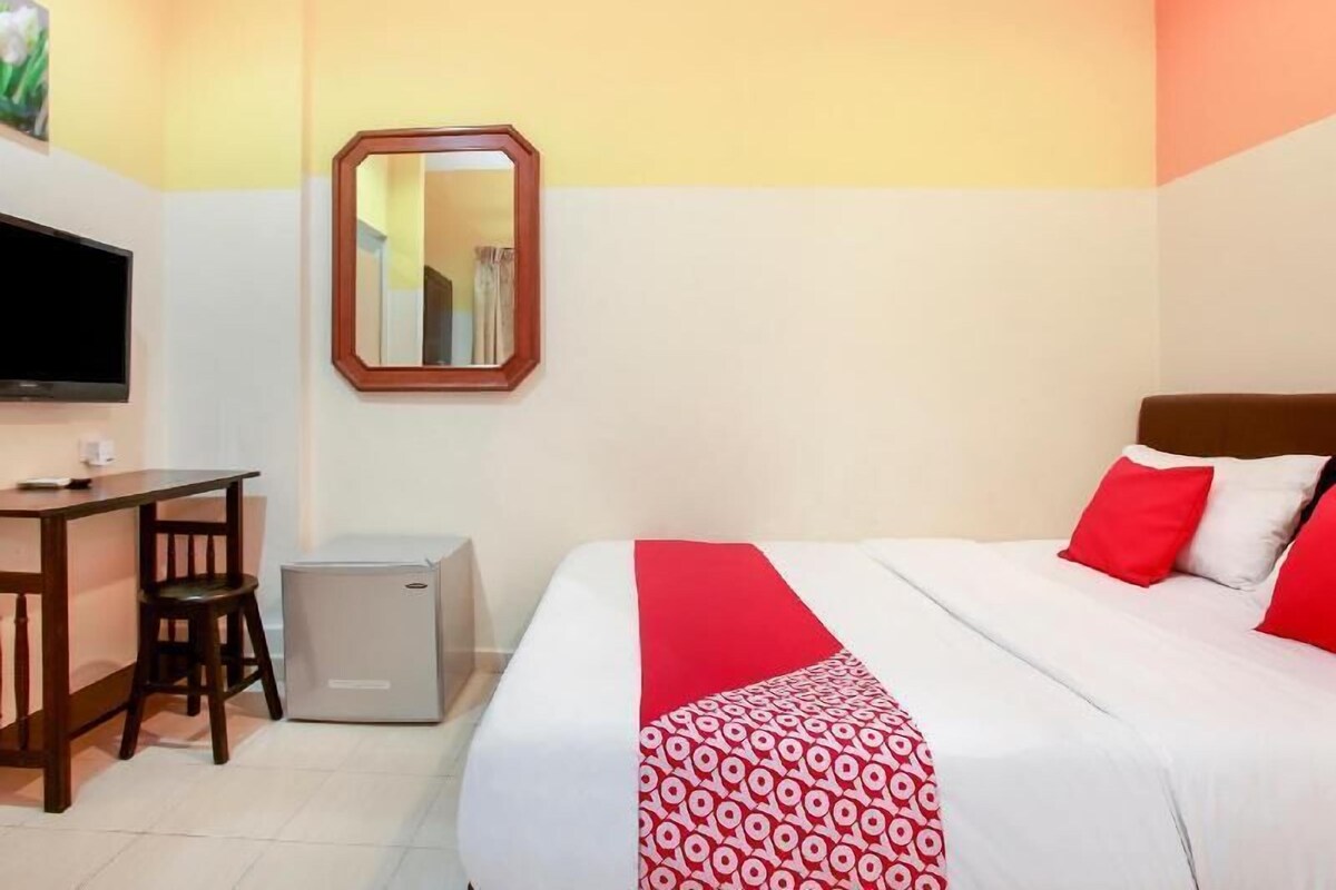 A hotel room with a bed, a desk, a chair, a small cabinet, and a television.
