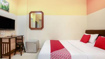 A hotel room with a bed, a desk, a chair, a small refrigerator, a TV, and a mirror.