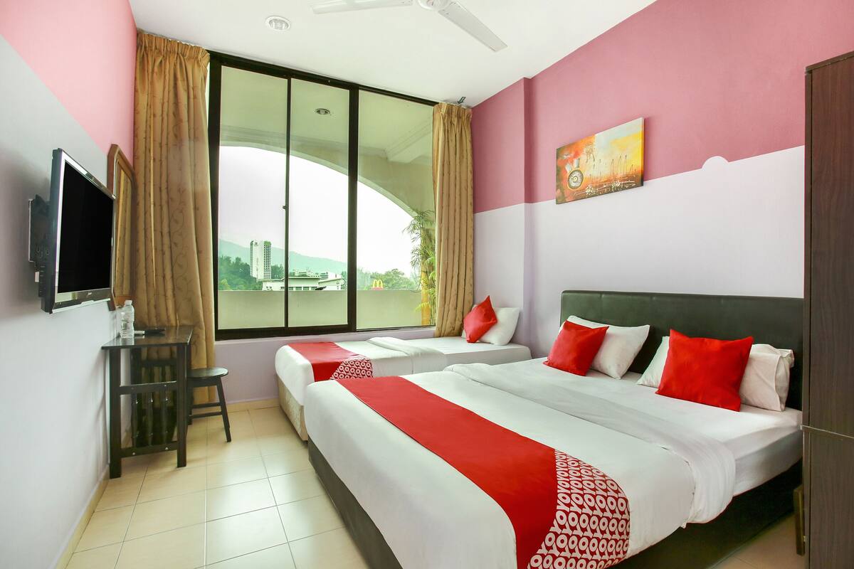 A hotel room with two beds, a TV, a desk, and a window with a city view.