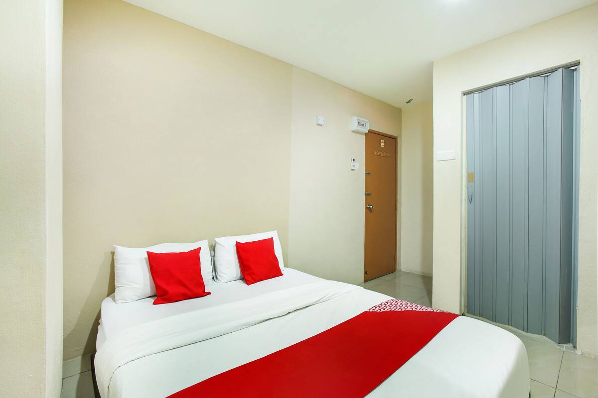 A hotel room with a bed, a red and white bedspread, and a closed door.