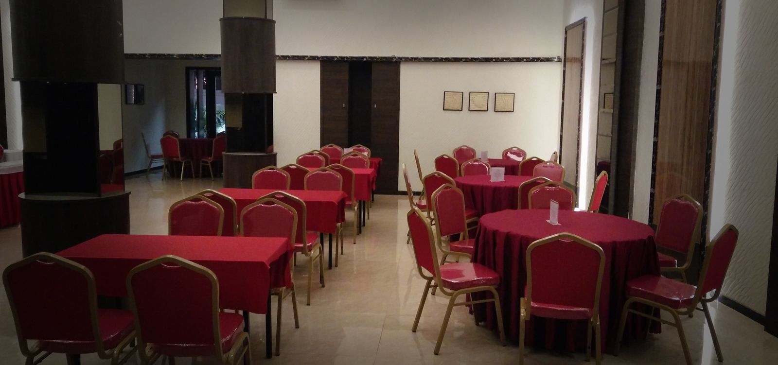 A conference room with multiple tables and chairs, a large pillar, and framed pictures on the wall.