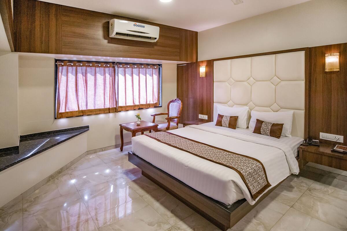 A hotel room with a large bed, a vanity with a mirror, a small table, and a window with curtains.