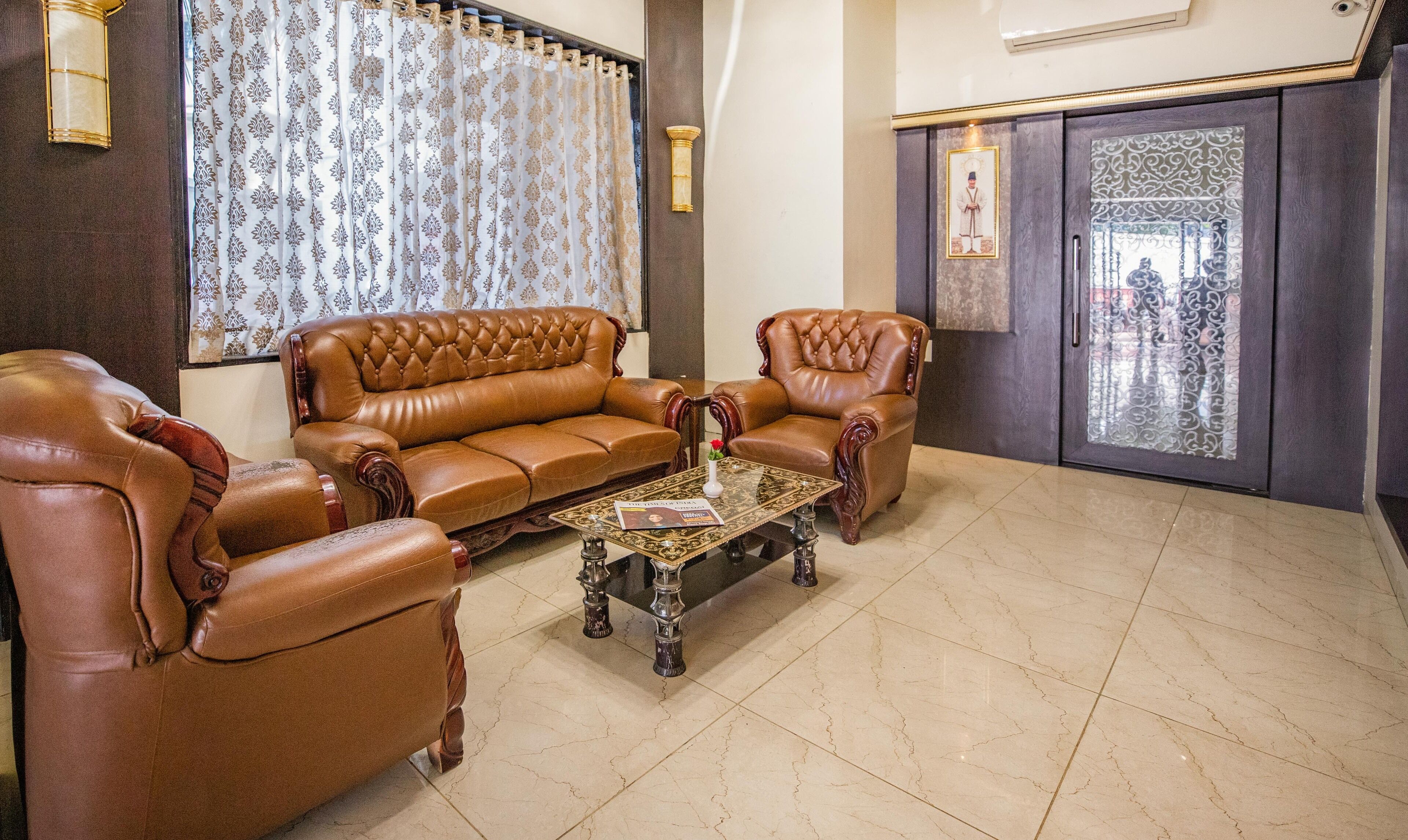 A living room with a brown leather sofa, two armchairs, and a glass coffee table.
