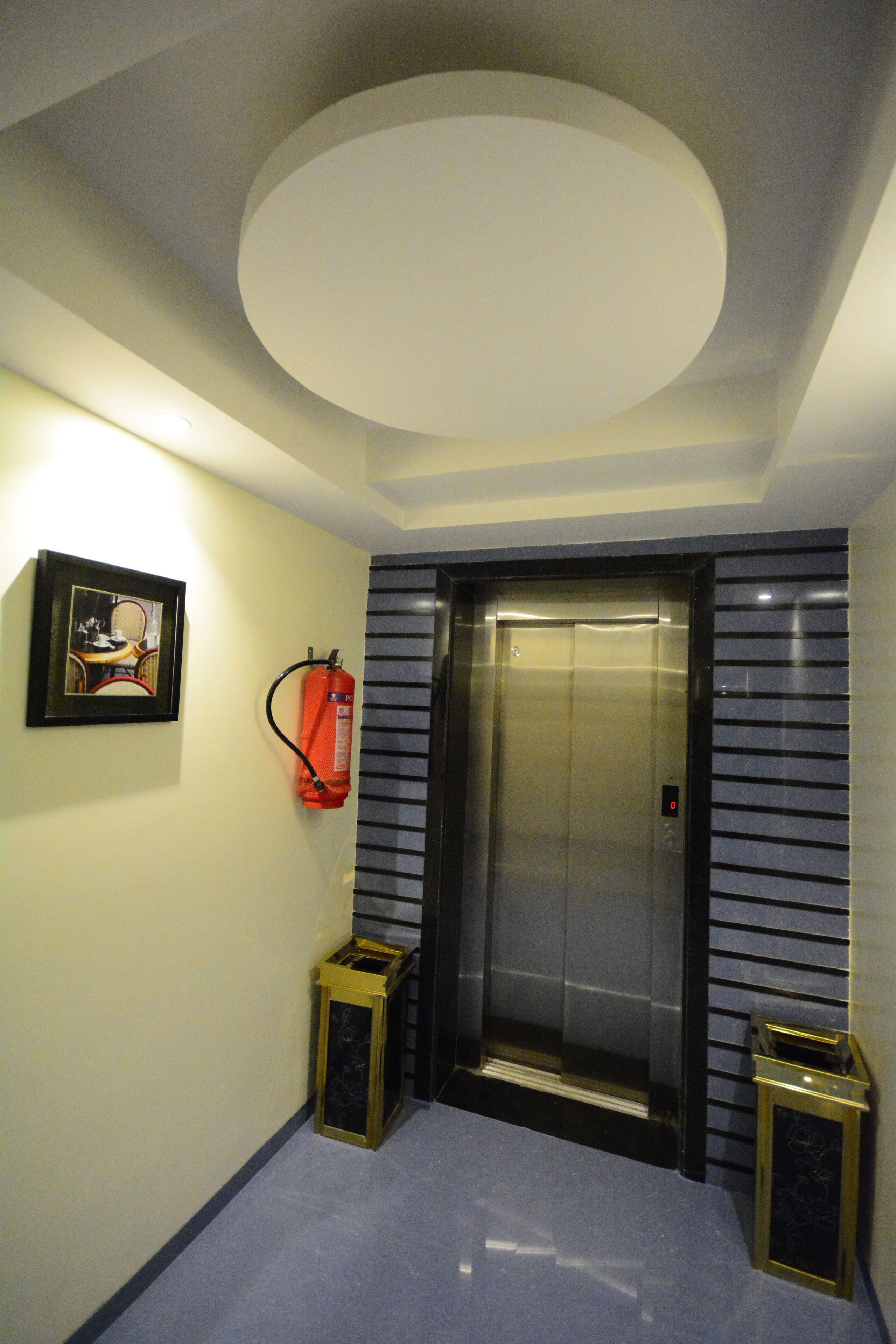 A hallway with a ceiling light, an elevator, a fire extinguisher, and two decorative lanterns.