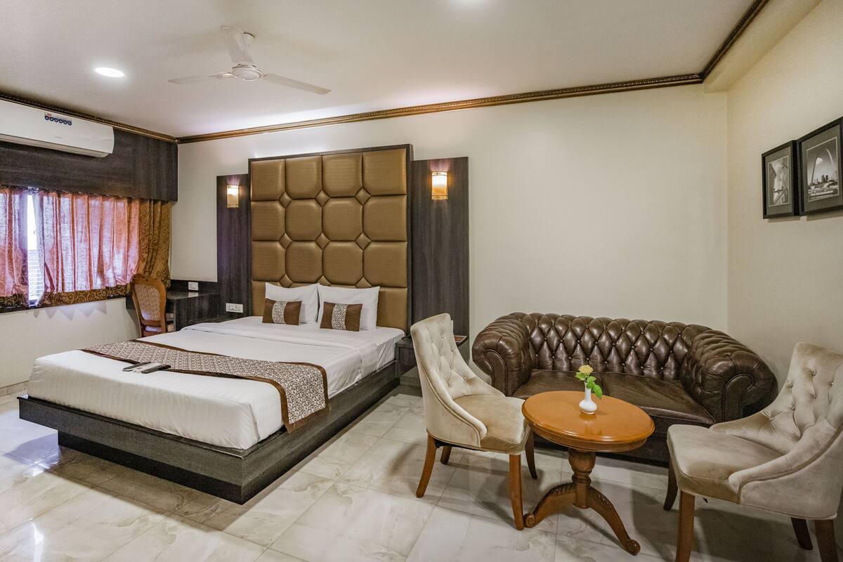 A hotel room with a large bed, a tufted headboard, a sofa, two armchairs, a small round table, and a ceiling fan.