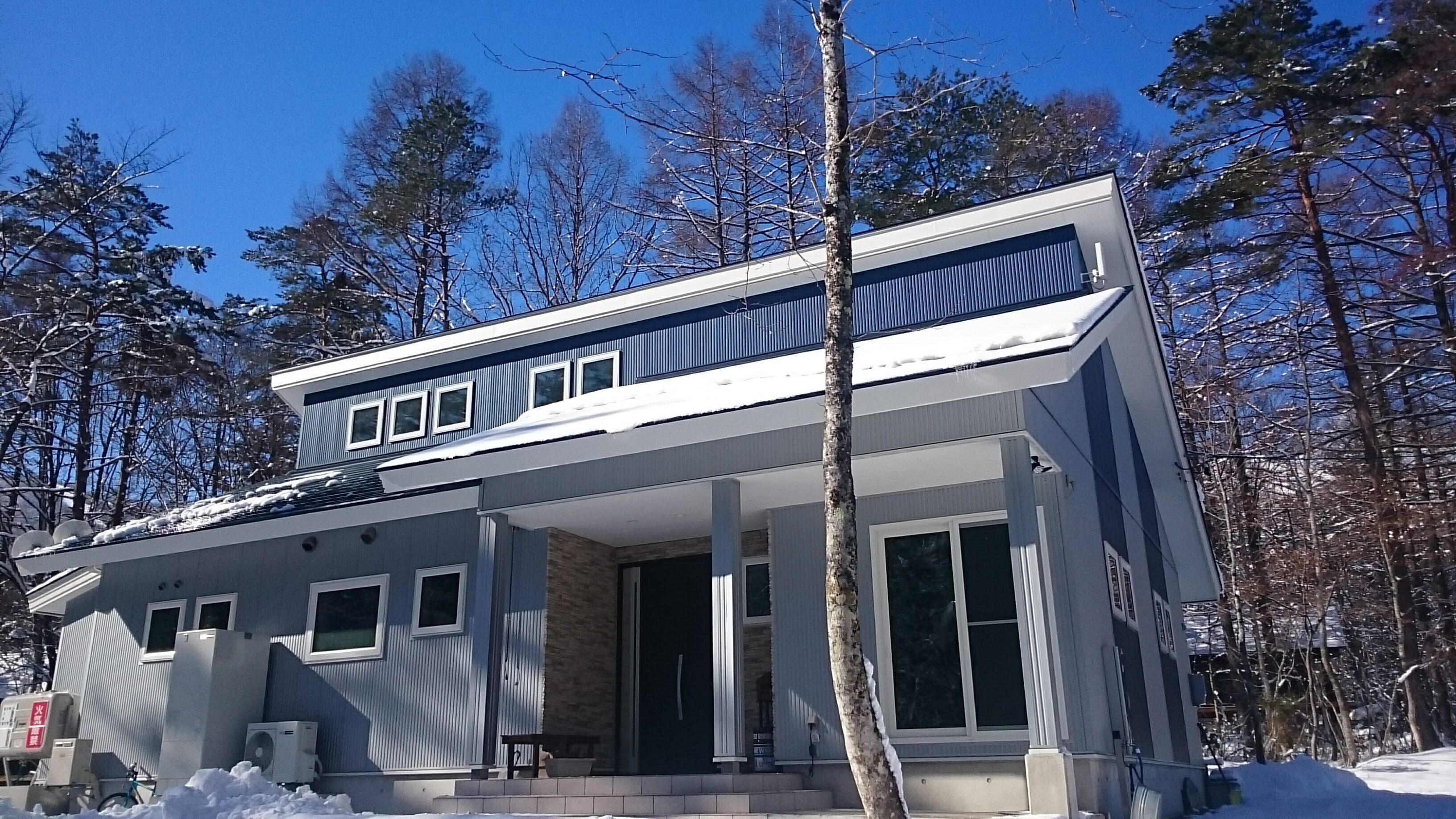 A modern two-story house with a covered porch, surrounded by snow-covered trees.