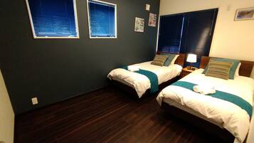 A hotel room with two single beds, dark wooden flooring, and two windows with blinds.