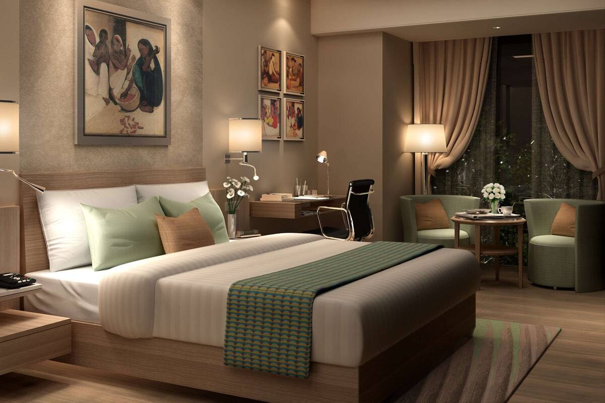 A modern hotel room with a large bed, bedside tables, a desk, two chairs, and a view of the outdoors.