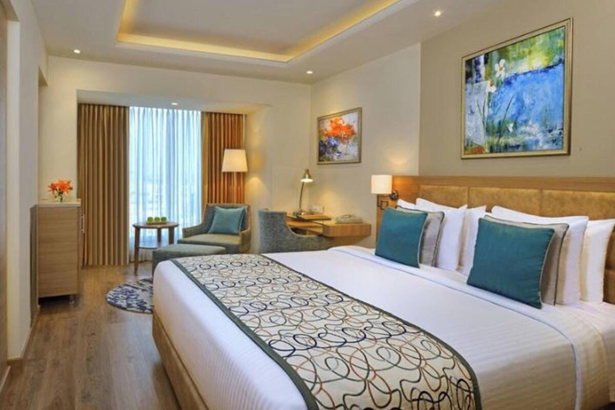 A hotel room with a bed, a desk, a chair, a TV, and a painting on the wall.