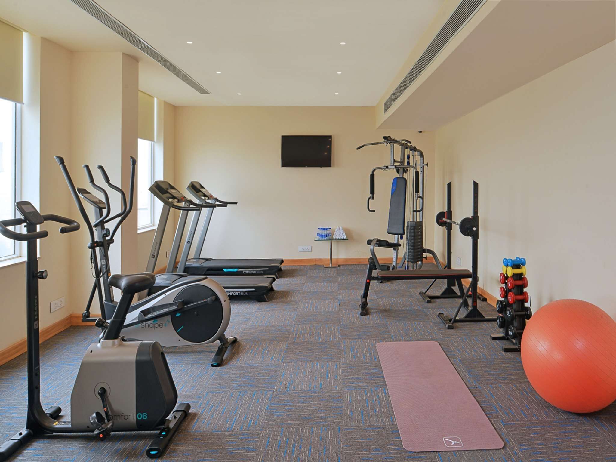 A fitness room with treadmills, an elliptical, a bench, a squat rack, and an exercise ball.