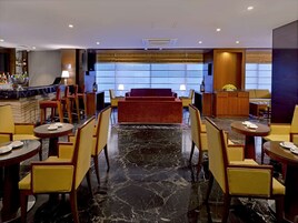 A hotel lobby with a bar area, seating with yellow chairs, a red sofa, and a marble floor.