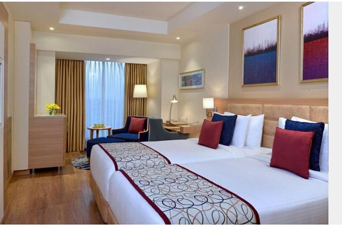 A hotel room with a large bed, a desk, a chair, a TV, and a painting on the wall.