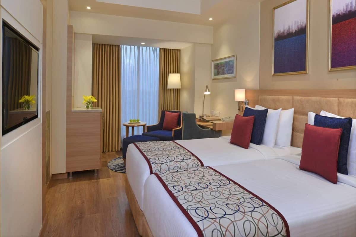 A hotel room with a large bed, a desk, a chair, a small table, and a window with curtains.