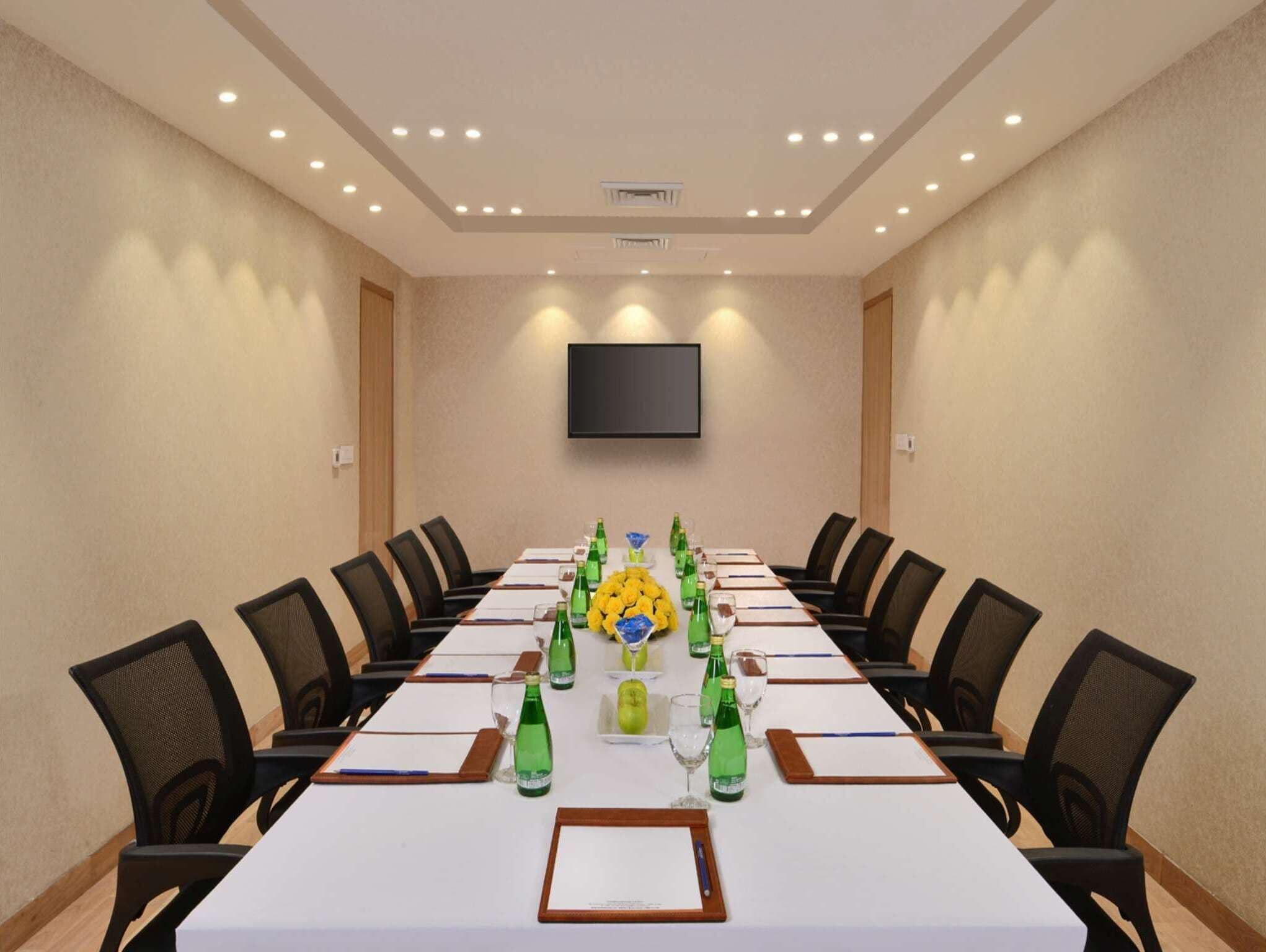 A conference room with a long table, chairs, a flat-screen TV, and a ceiling light fixture.