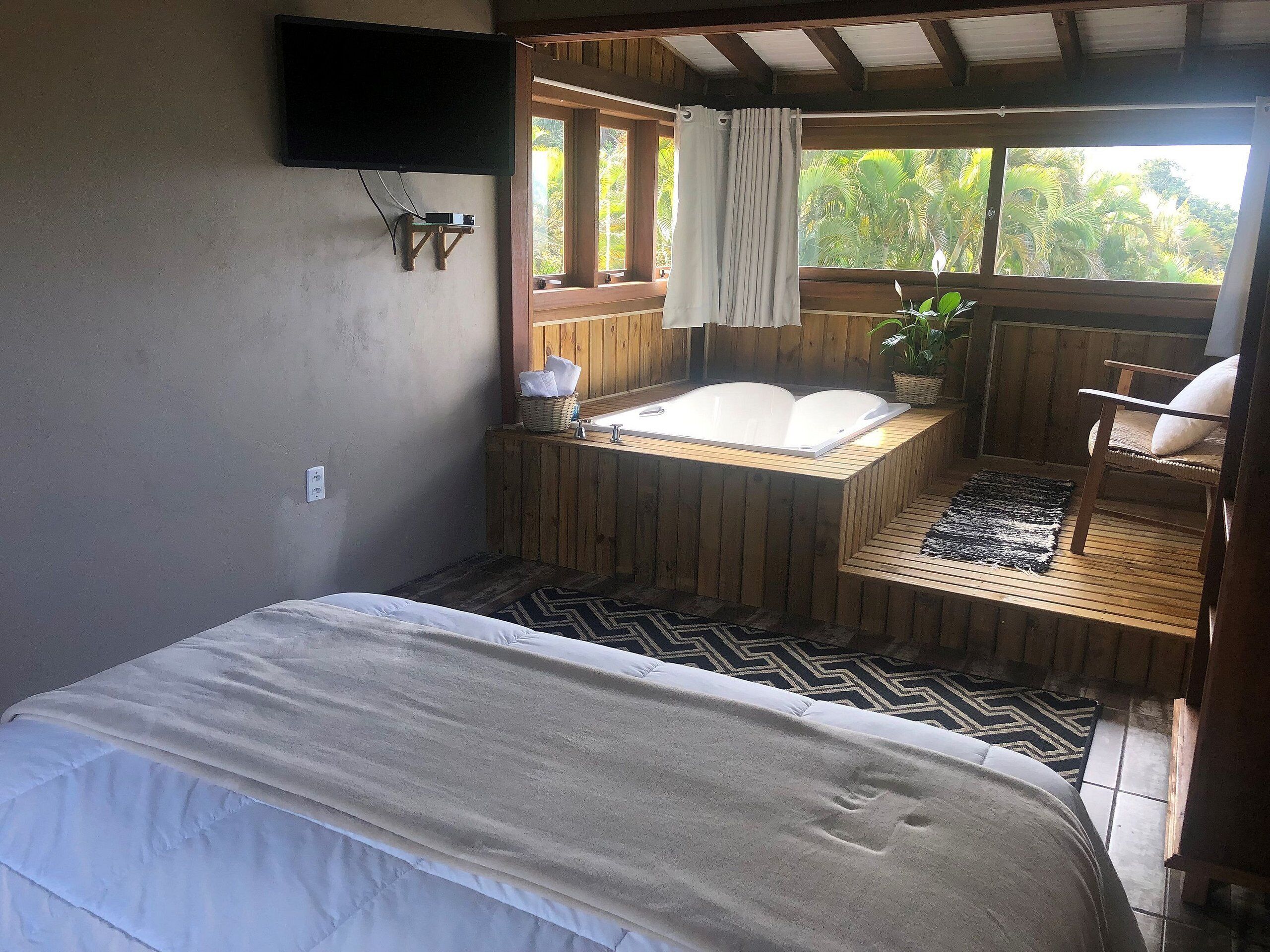 Una habitación con cama, una bañera de madera, una silla y un ventanal con cortinas.