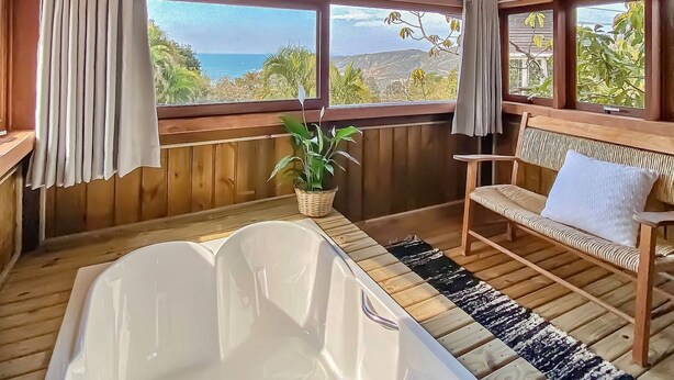 A wooden cabin with a large bathtub, a bench, and a view of the ocean. - Studios do Barão (Imbituba)