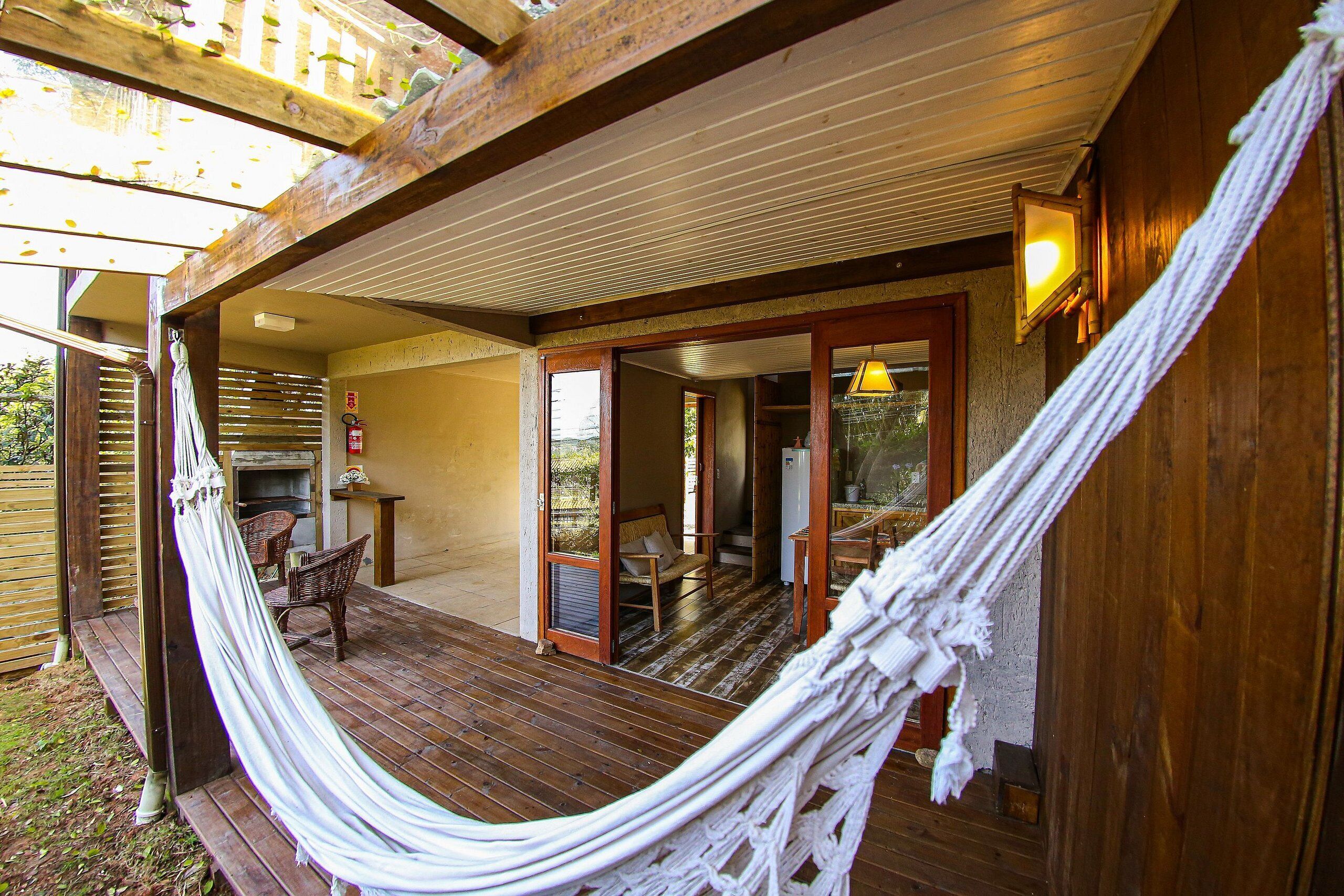 Una terraza de madera con una hamaca, muebles de madera y un ventanal corredera que da a un espacio interior.