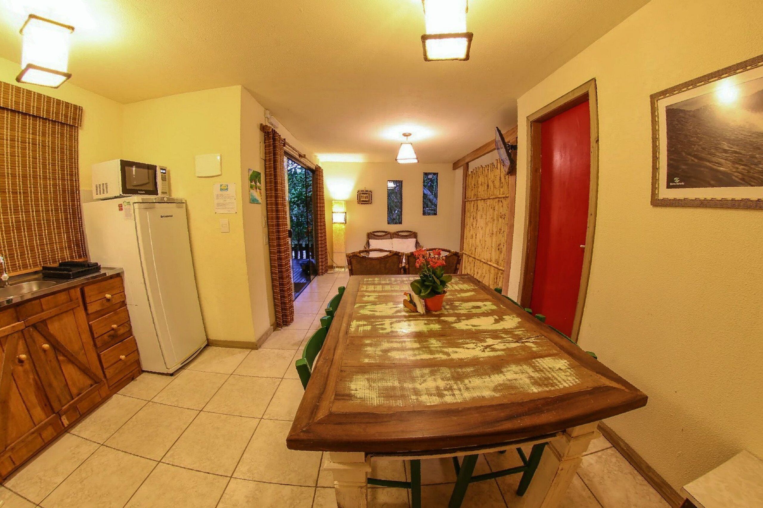 Una cocina compacta con microondas, refrigerador y gabinetes de madera. Una mesa de comedor con sillas está ubicada en el centro.