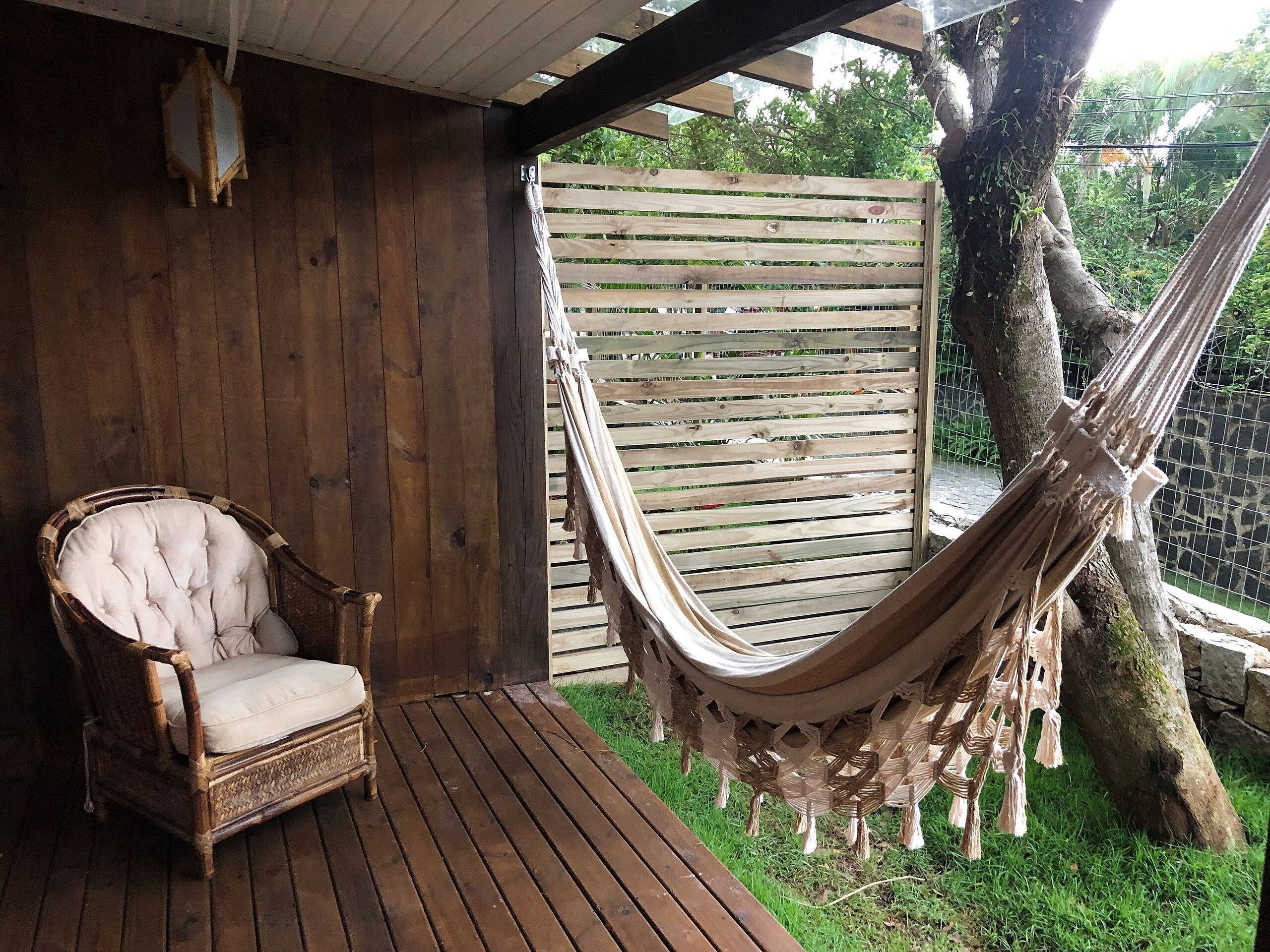 Une terrasse en bois avec une chaise en osier et un hamac.