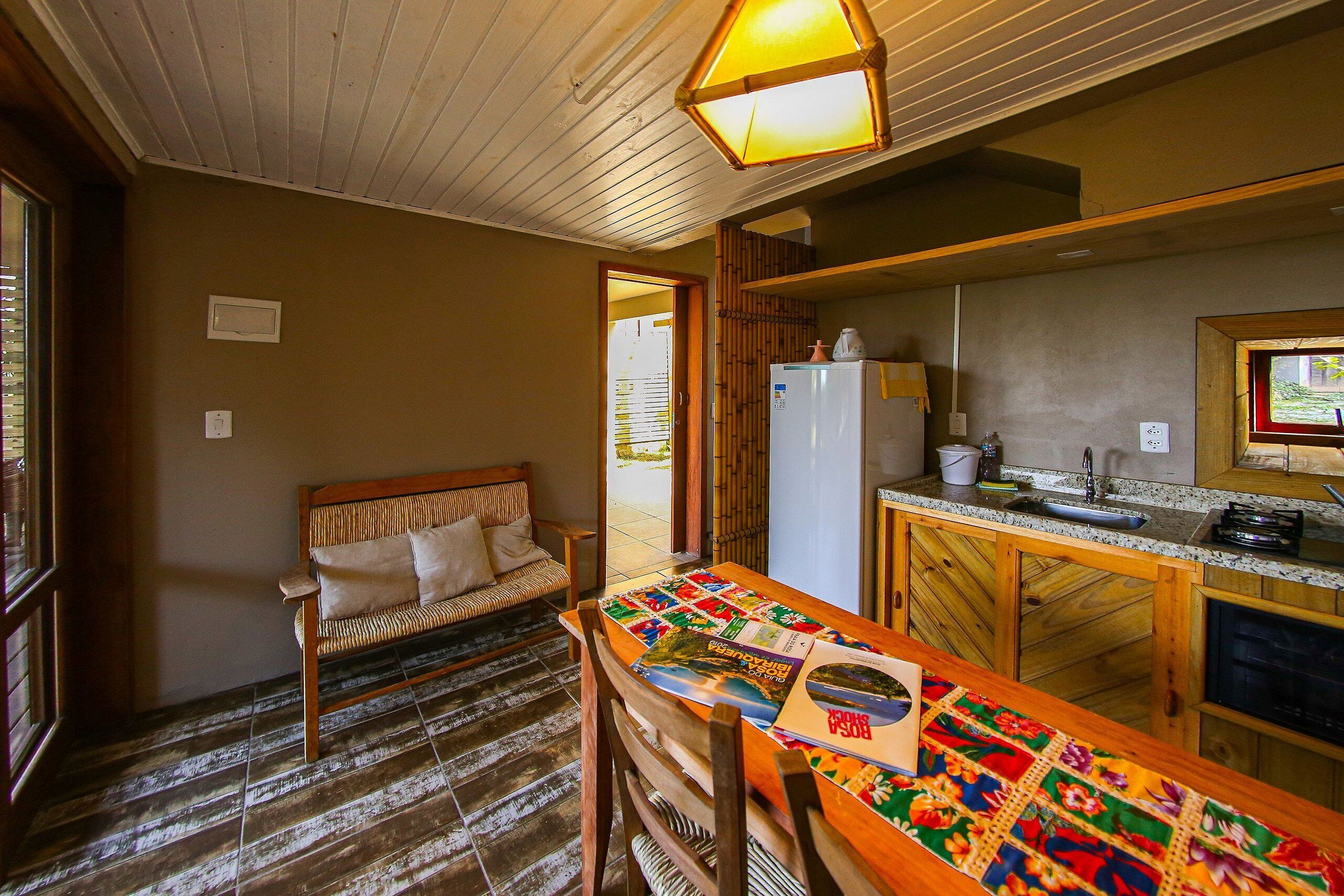 A compact kitchen with wooden cabinets, a refrigerator, and a dining area with a table covered in a colorful tablecloth.