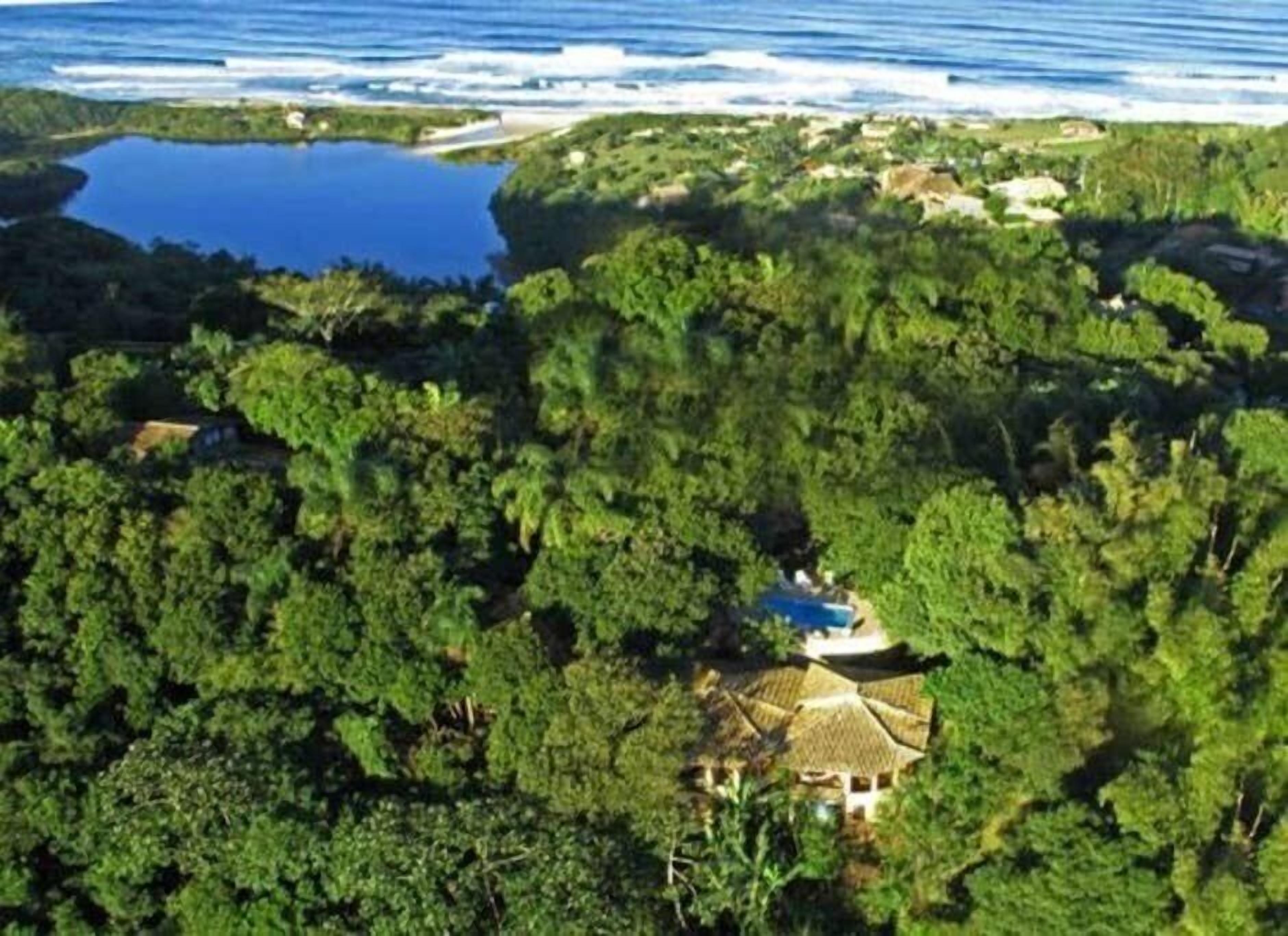 A secluded resort with a central building surrounded by dense forest, a small lake, and a beach.