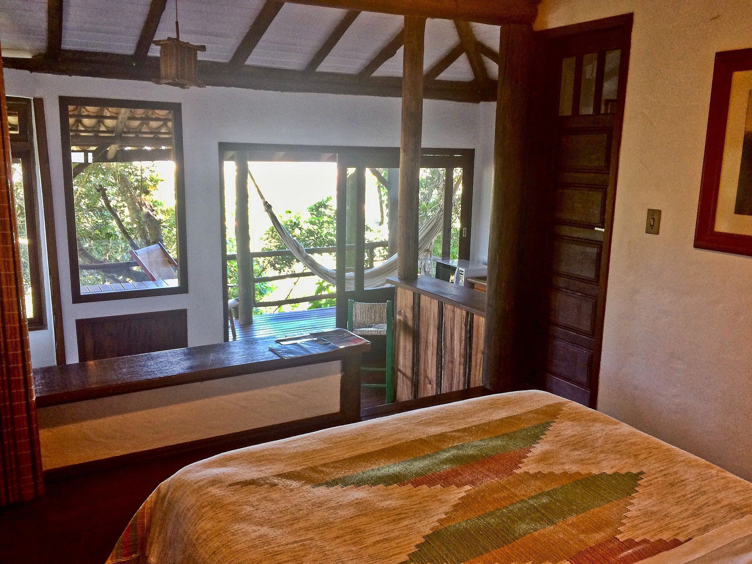 Una habitación con una cama, un escritorio de madera y vistas al verdor exterior.