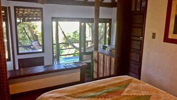 Una habitación con una cama, un escritorio de madera y vistas al verdor exterior.