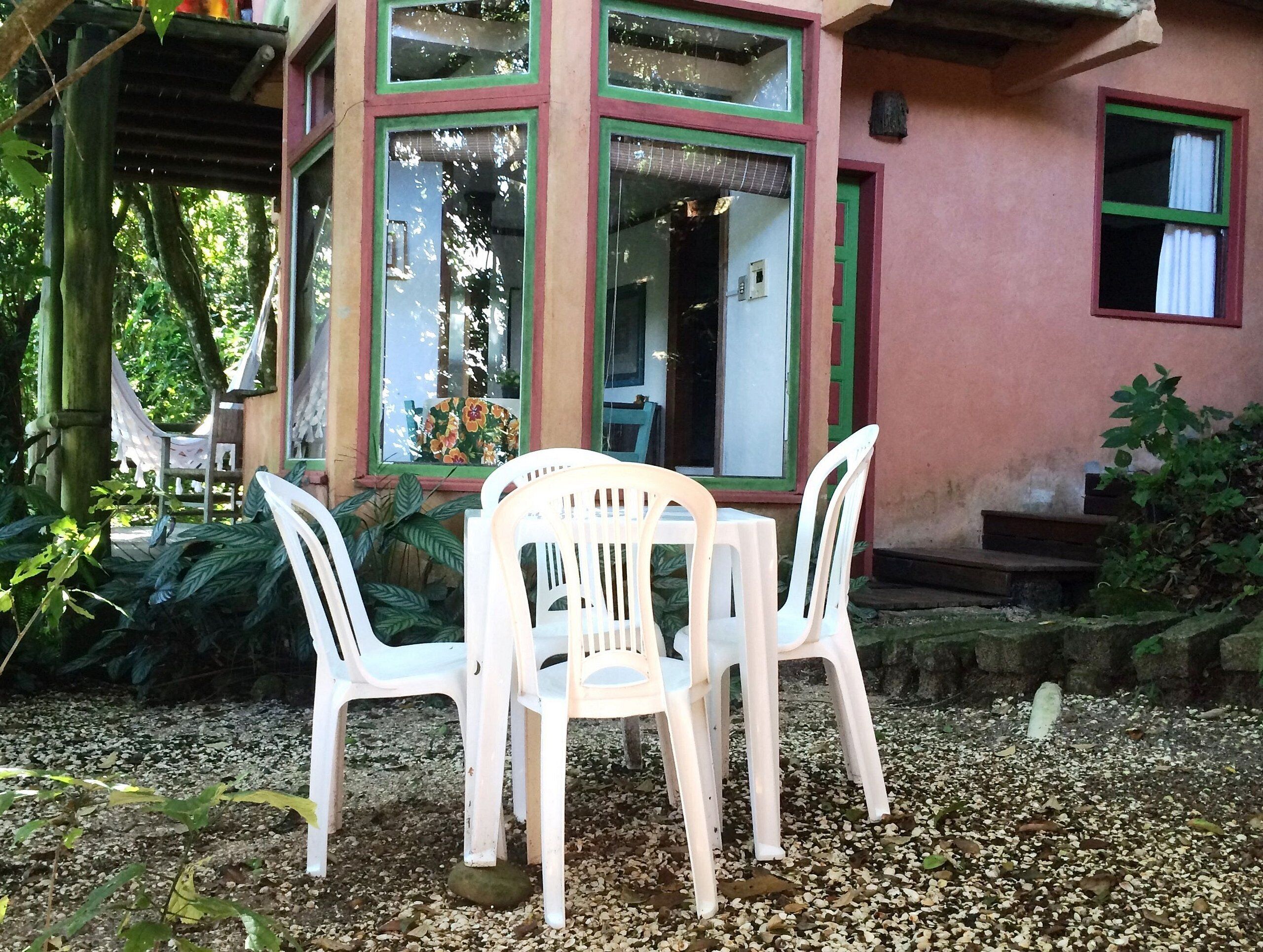 A small outdoor seating area with a table and chairs, surrounded by a garden with plants and a gravel path.