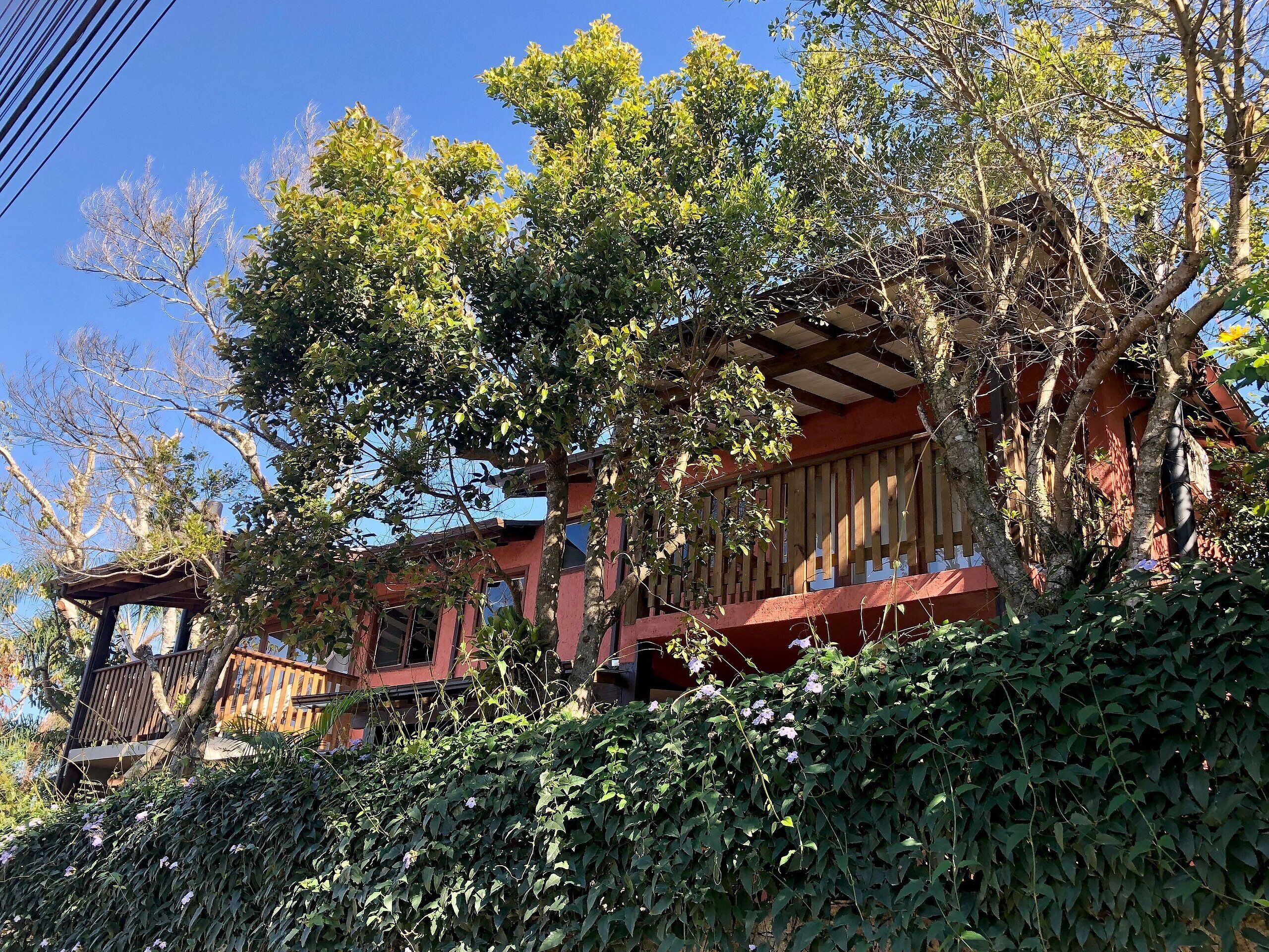 Un edificio de madera tradicional con fachada roja, rodeado de abundante vegetación y árboles.