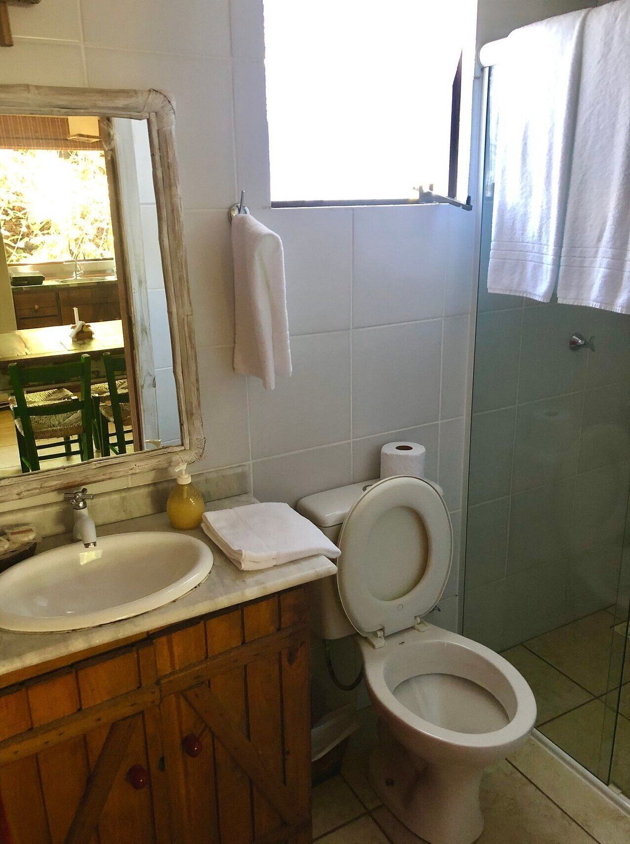 Un baño con tocador de madera, lavamanos, inodoro y espejo.
