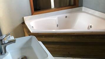 A bathroom with a white sink, a wooden bathtub, and a mirror above the sink.