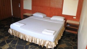 A hotel room with a large bed, two bedside tables, a wooden wardrobe, and a stone floor.