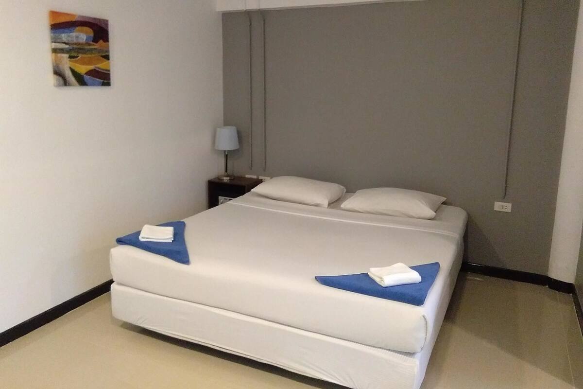 A hotel room with a bed, a nightstand, a lamp, and a painting on the wall.