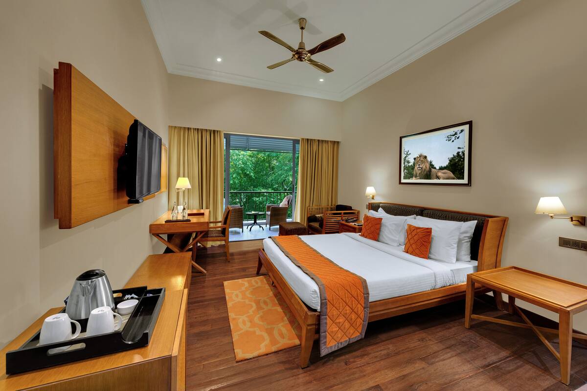 A hotel room with a bed, bedside table, desk, chair, and a balcony with curtains.