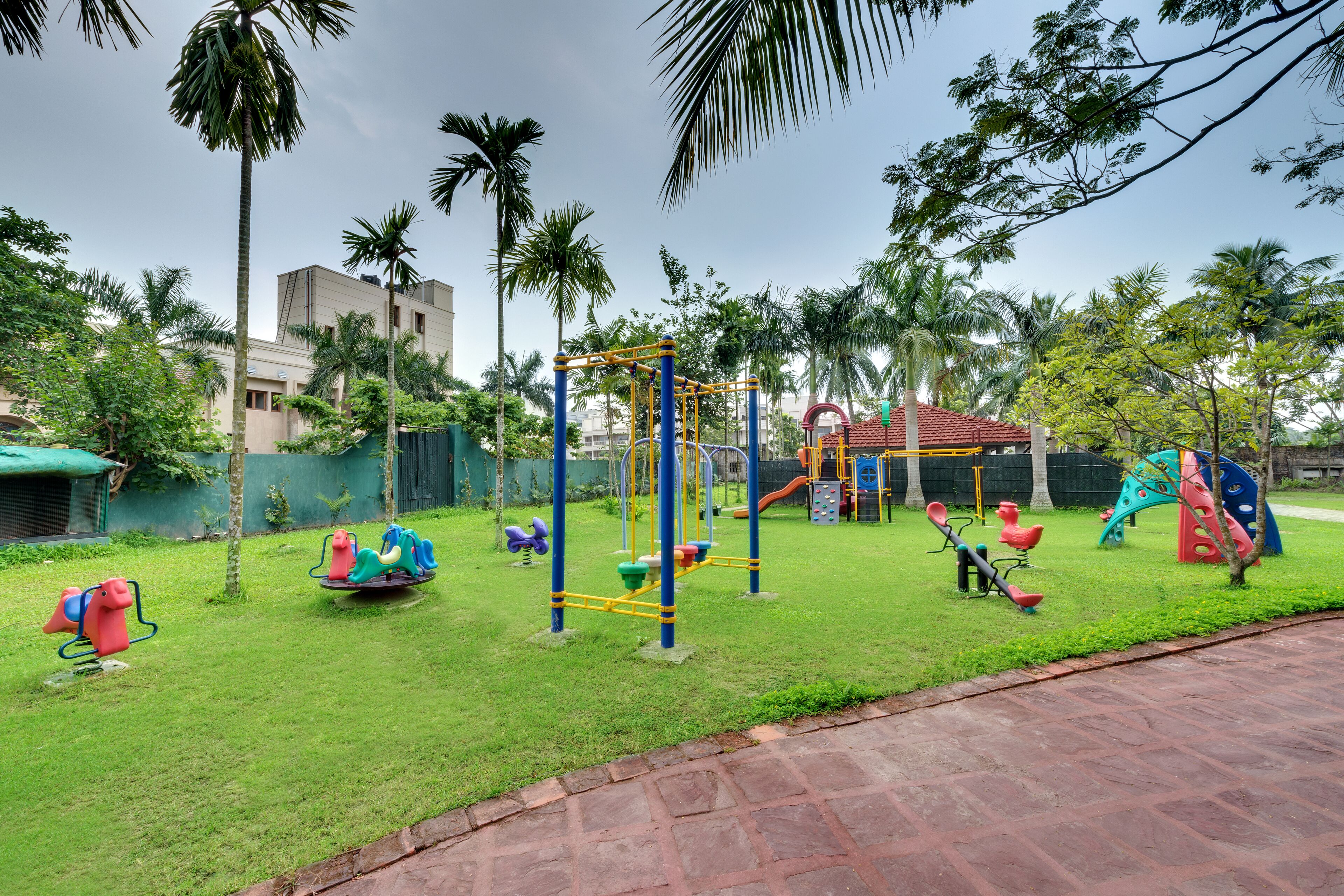 A playground with various play equipment, surrounded by grass and palm trees.